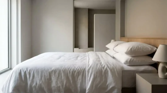 Perfectly made luxury hotel bed with crisp white linens and plush pillows bathed in soft natural window light